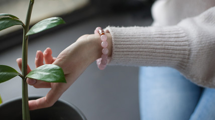 the girl has rose quartz bracelets, the girl is holding a branch with green leaves, the girl is holding a indoor flower (horizontally, close up).