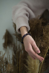 a girl with bracelets of amethyst hands on a bouquet of dry grass