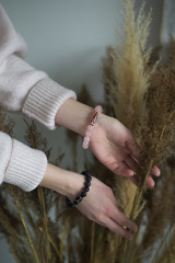 a girl with rose quartz and amethyst bracelets holds a bouquet of dry grass, the girl has bracelets on her hands (vertically).