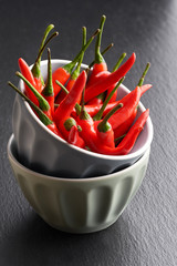 Red hot chili peppers in a stack of two grey ceramic bowls on dark grey slate stone