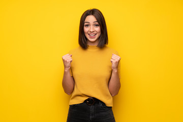 Young woman over yellow wall celebrating a victory in winner position
