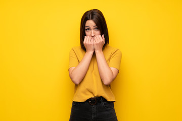 Young woman over yellow wall nervous and scared putting hands to mouth