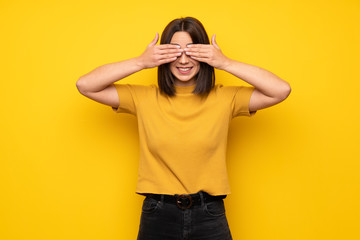 Young woman over yellow wall covering eyes by hands. Surprised to see what is ahead