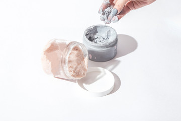 Natural face and body mask and Face and body Skin Scrub in containers and woman hand on a light background with a shadow.  