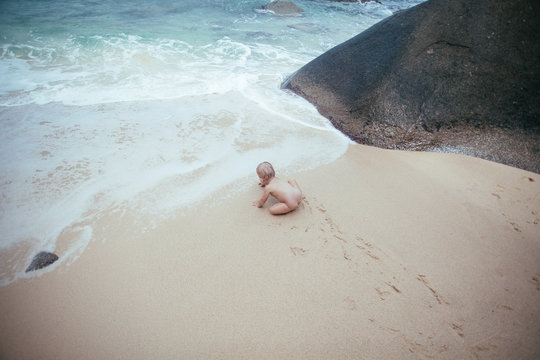 Overhead view of a naked baby girl playing on the beach, Seychelles
