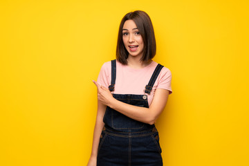 Young woman over yellow wall pointing to the side to present a product