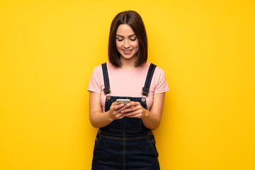 Young woman over yellow wall sending a message with the mobile