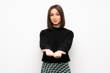 Fototapeta premium Young woman over white wall holding copyspace imaginary on the palm to insert an ad