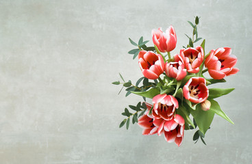 Bunch of red tulips and eucalyptus leaves on grey background, top view, text space