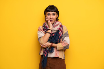 Young hippie woman over yellow wall surprised and shocked while looking right