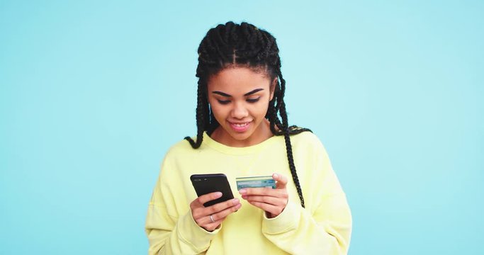 Good looking african woman make a online transaction with her smartphone , using the credit card , in a studio with a blue background wall. 4k