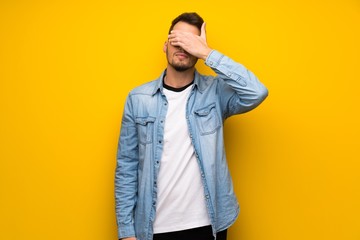 Handsome man over yellow wall covering eyes by hands. Do not want to see something