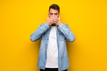 Handsome man over yellow wall covering mouth with hands for saying something inappropriate