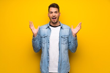 Handsome man over yellow wall with shocked facial expression