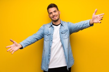 Handsome man over yellow wall presenting and inviting to come with hand