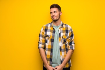 Handsome man over yellow wall looking to the side