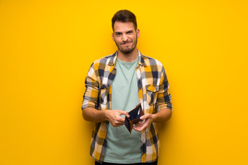 Handsome man over yellow wall holding a wallet - obrazy, fototapety, plakaty