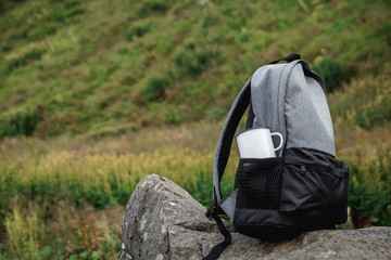 A backpack, a mug, a notepad and a map are lying on the grass. Tourist equipment. The apple lies in the pocket of the backpack. Walk in the forest. Camping in the mountains