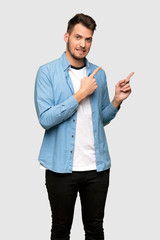 Handsome man frightened and pointing to the side over grey background