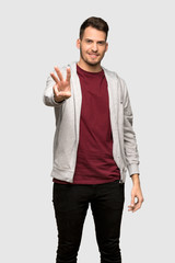 Man with sweatshirt happy and counting three with fingers over grey background