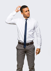 Young afro american businessman having doubts while scratching head on isolated background