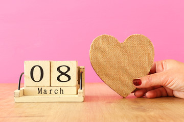 wooden March 8 calendar next to heart over pink wooden background