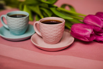 Two cup of coffe with a pink tulips over pink background.