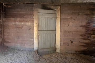 Grey wooden door highlighting wood paneled wall with dirt covered floor