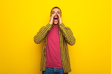 Young afro american man on yellow background shouting and announcing something