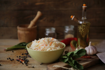 sauerkraut in a bowl on a wooden table with olive oil in a bottle, spices, garlic and herbs. Healthy food.