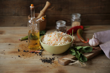 sauerkraut in a bowl on a wooden table with oil in a bottle, spices and herbs