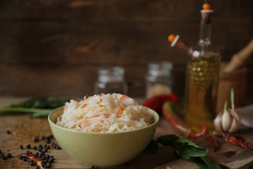 sauerkraut in a bowl on a wooden table with olive oil in a bottle, spices, garlic and herbs. Healthy food.