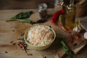 sauerkraut in a bowl on a wooden table with oil in a bottle, spices and herbs