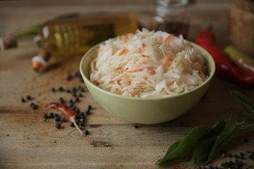  sauerkraut in a bowl on a wooden table with oil in a bottle, spices and herbs