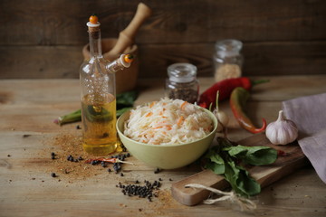 sauerkraut in a bowl on a wooden table with oil in a bottle, spices and herbs