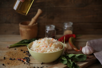 pouring olive oil into a bowl of sauerkraut on a wooden table with spices and herbs