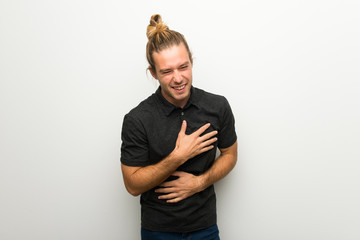 Blond man with long hair over white wall smiling a lot while putting hands on chest