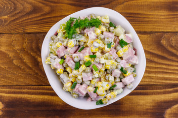 Tasty salad with sausage, green pea, canned corn, bell pepper, cucumber and mayonnaise on wooden table. Top view