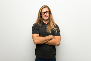 Blond man with long hair over white wall with glasses and happy