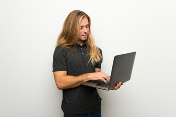 Naklejka premium Blond man with long hair over white wall with laptop