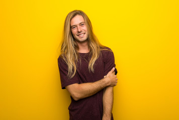 Blond man with long hair over yellow wall With happy expression