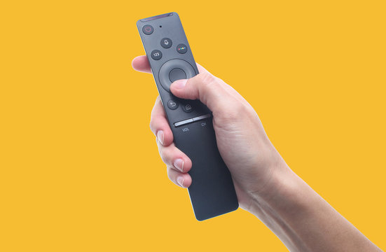 Hand holds tv remote isolated on yellow background