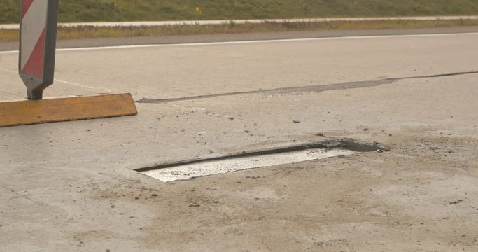 Closeup of pit in asphalt road repaired with concrete patch at road construction site. Road works concept. Teamwork. Group of workers on a road construction. Team of people at work.
