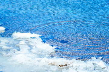 Berih river with remnants of snow and ice. Water is very clean and clear, through it the bottom of the river is visible. Blue water