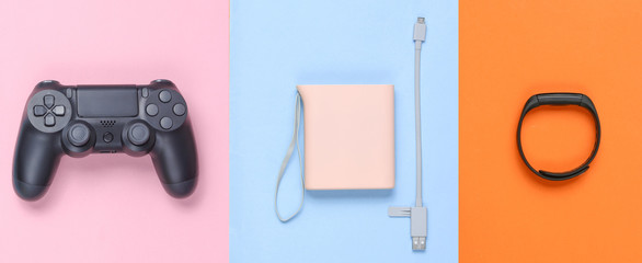 Power bank and usb cable, gamepad, smart bracelet on colored pastel background. Modern gadgets. Top view, minimalism..