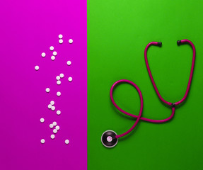 Stethoscope, pills on pink green background. Medical concept, top view