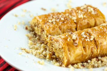 Two pieces of golden, flaky baklava on a white plate, garnished with crushed nuts, set against a vibrant red and gold striped background.