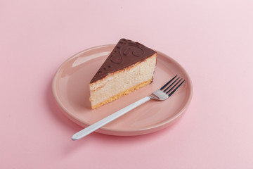 A piece of cake, cheesecake on a plate with a fork on a pink background.