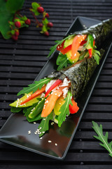 Sushi temaki with rice on a black plate. Decorative branch plants.