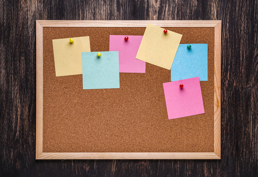 corkboard with pinned multicolored stickers on dark  background